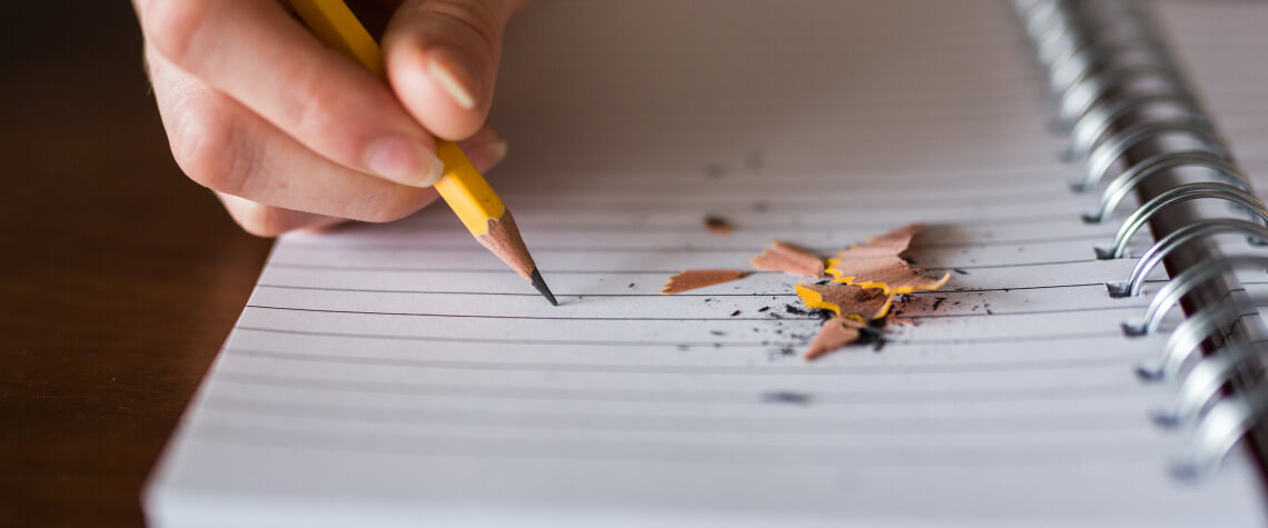 Foto de mão escrevendo com lápis em um caderno pautado